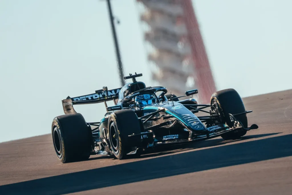 A black and teal Formula 1 car driving on an asphalt track with a tower structure in the blurred background.