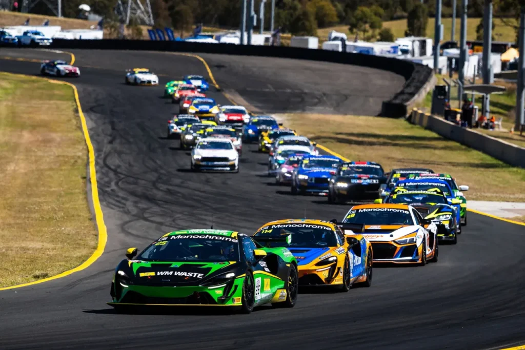 A pack of GT4 race cars cornering on an asphalt circuit.