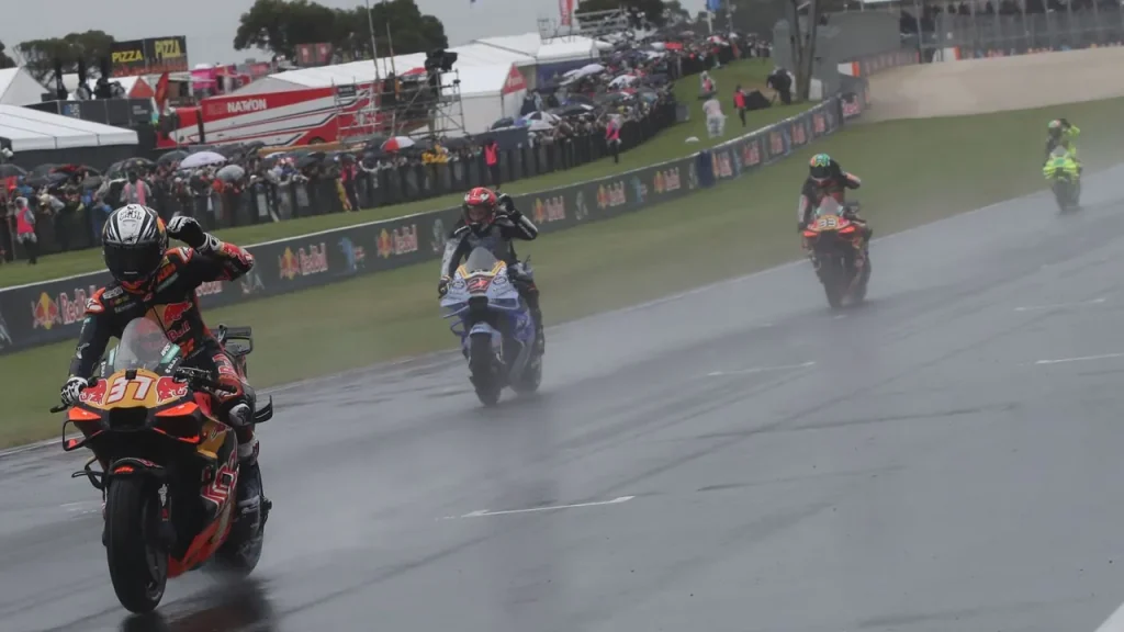 A motorcycle racer leads other competitors down a wet race track under rainy conditions.