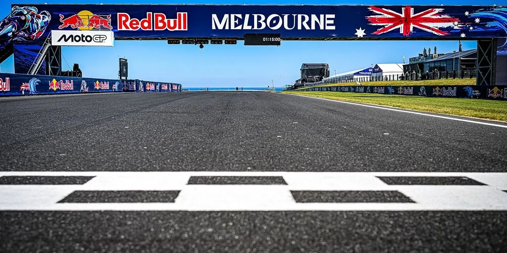 An empty race track straight extends from the start-finish line beneath an overhead gantry.