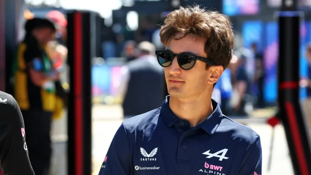 A man wearing sunglasses and a navy Alpine team polo shirt outdoors.