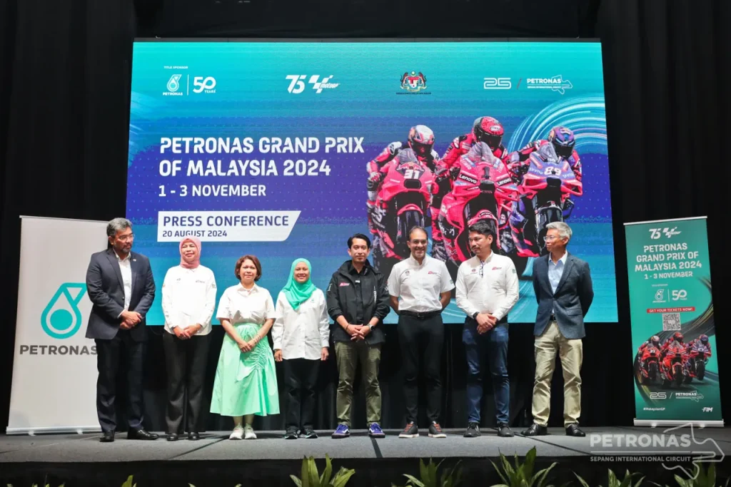 A group of people standing on a stage in front of a press conference backdrop screen displaying racing motorcycles.