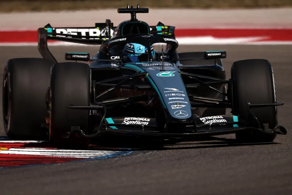 A black and teal Formula 1 car driving on a racetrack over a kerb.