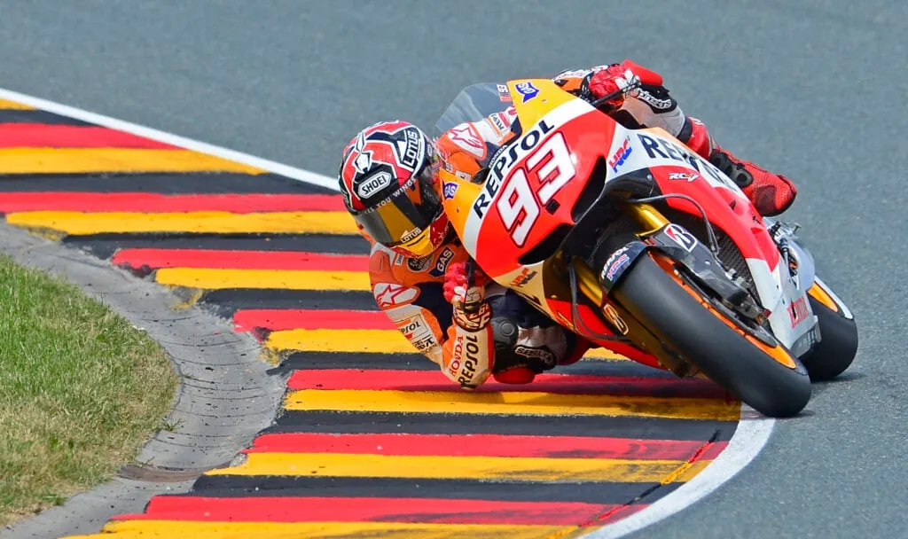 A motorcycle racer leaning sharply through a corner on a paved racetrack beside striped kerbing.