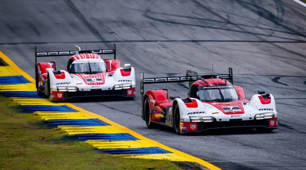 Two red and white prototype race cars on an asphalt track with yellow and blue curbing.