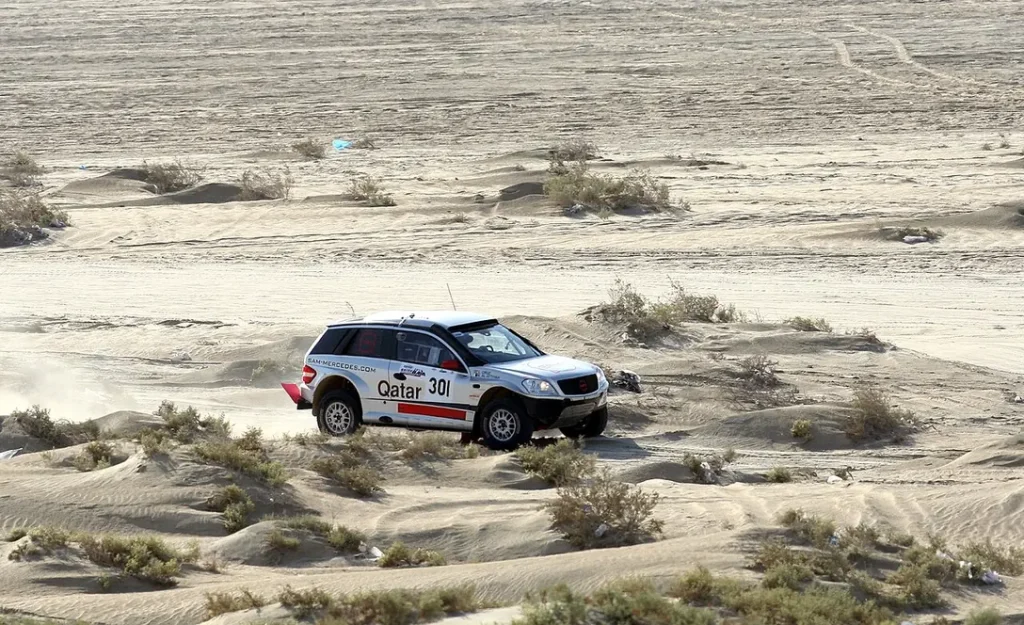Nasser Saleh Al-Attiyah’s white rally SUV crosses sandy desert terrain dotted with shrubs during the 2011 Qatar International Baja.