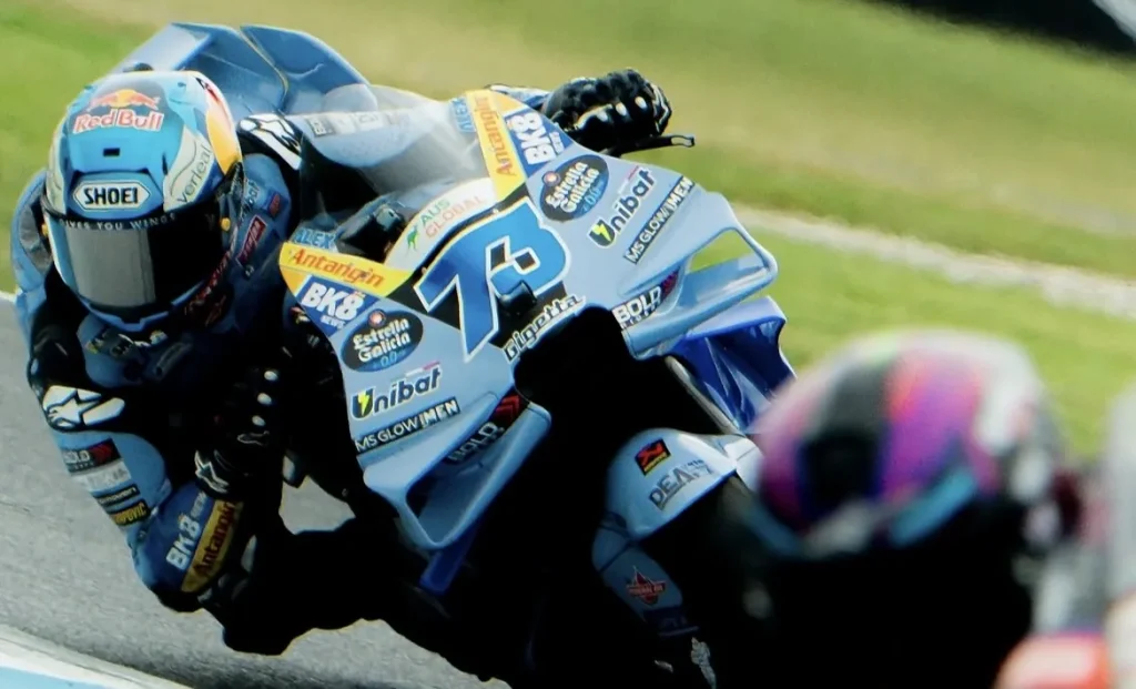 A motorcycle racer leaning into a turn on a blue racing motorcycle on an asphalt track.