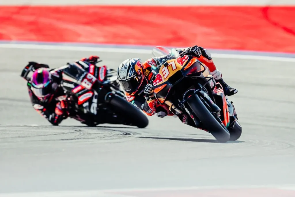 A motorcycle racer leaning into a corner on a circuit followed closely by another rider.