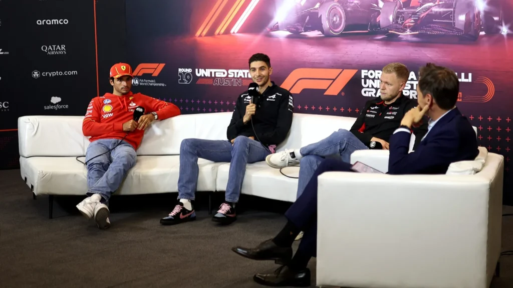 Drivers seated on white sofas with microphones face an interviewer against a United States Grand Prix backdrop.
