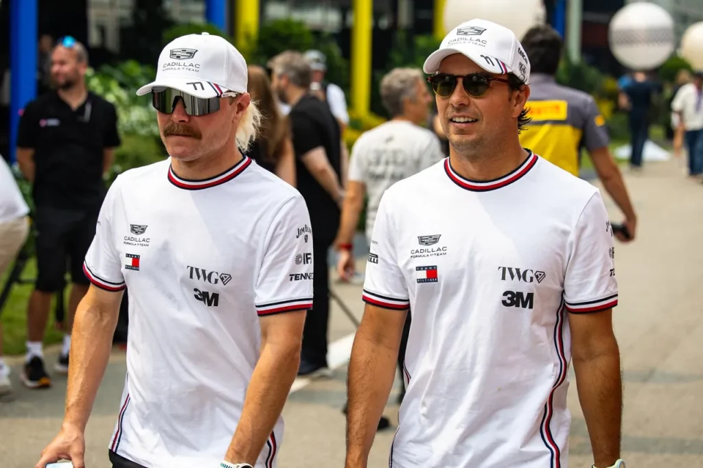 Two men wearing white Cadillac team shirts, white baseball caps, and sunglasses walking side by side.