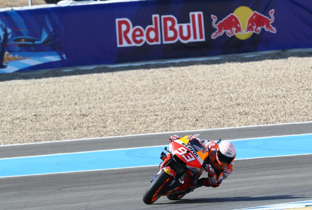 Rider leaning a Repsol Honda motorcycle numbered 93 through a corner, with blue runoff and gravel behind.