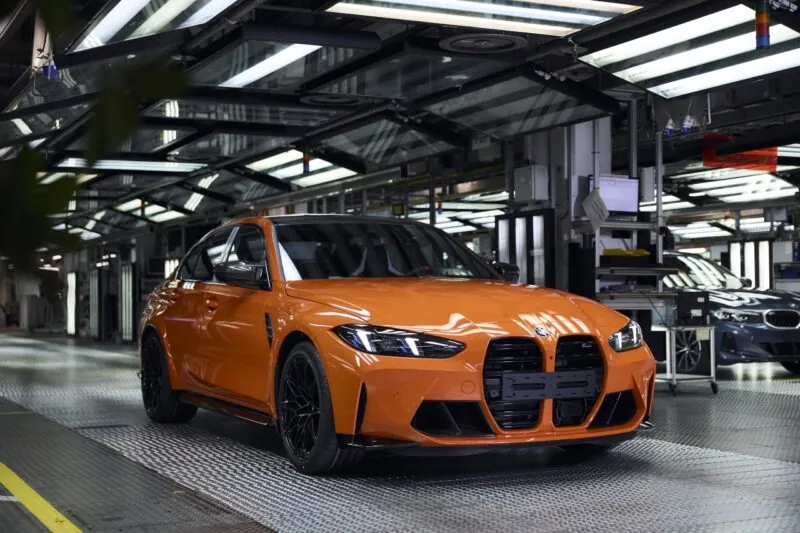 An orange BMW sedan on an automotive factory assembly line under overhead lights.