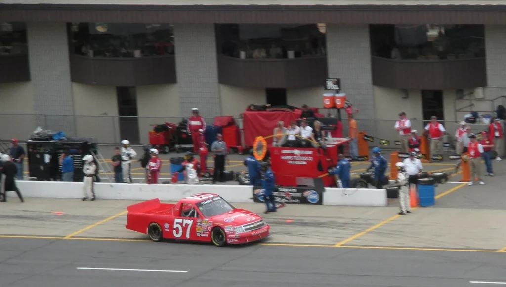 Red No. 57 Chevrolet racing truck on pit road, with crews and pit equipment behind it.