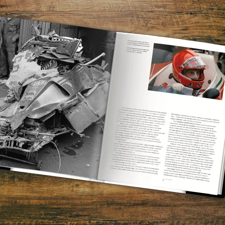 Open book on a wooden surface showing a damaged racing car on the left page and a driver wearing a helmet on the right page.