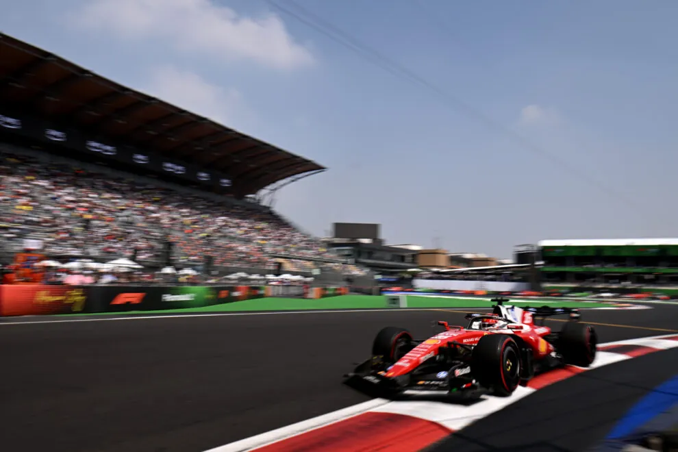 A red Formula 1 car driving on a racetrack in front of a large spectator grandstand.