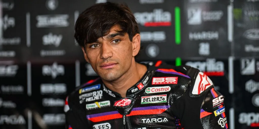 A motorcycle racer wearing racing leathers looks ahead inside a pit garage.