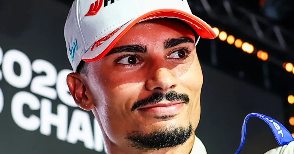 A close-up portrait of a smiling man with a mustache and goatee wearing a white cap.