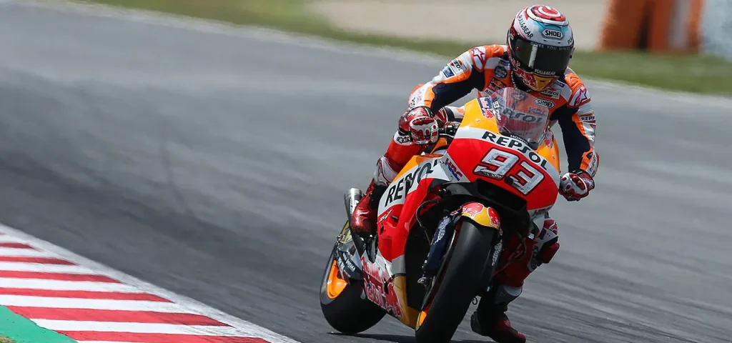Marc Márquez riding the #93 Repsol Honda MotoGP motorcycle, leaning into a corner on an asphalt circuit alongside red-and-white striped kerbing. The rider is wearing branded Repsol Honda leathers and a helmet, with visible Honda, Repsol, and Red Bull liveries.