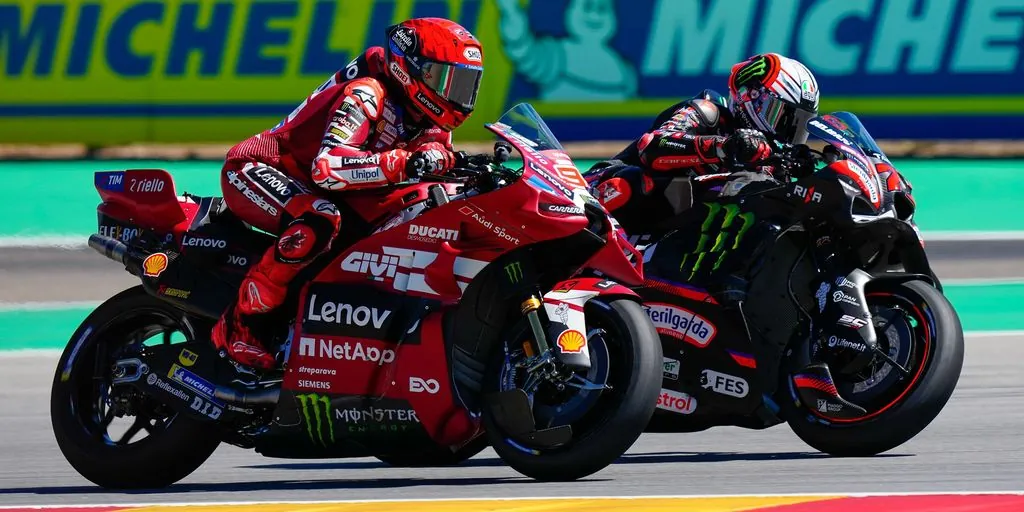 MotoGP riders leaning through a corner on a racetrack in front of Michelin trackside signage.