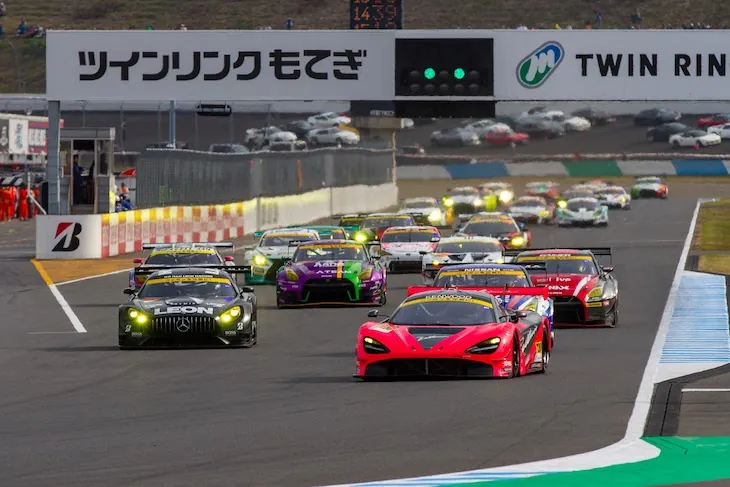 A pack of GT race cars speeds down the main straight during a race.