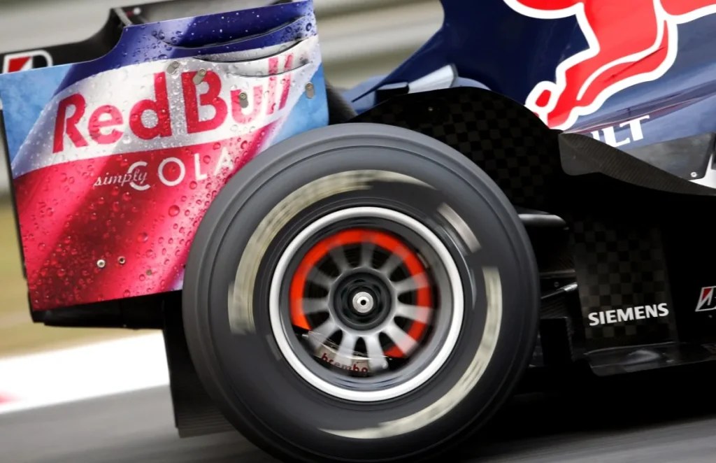 Close-up of a Red Bull-liveried Formula 1 car’s wheel, showing a red-orange glowing brake disc behind the blurred spokes.